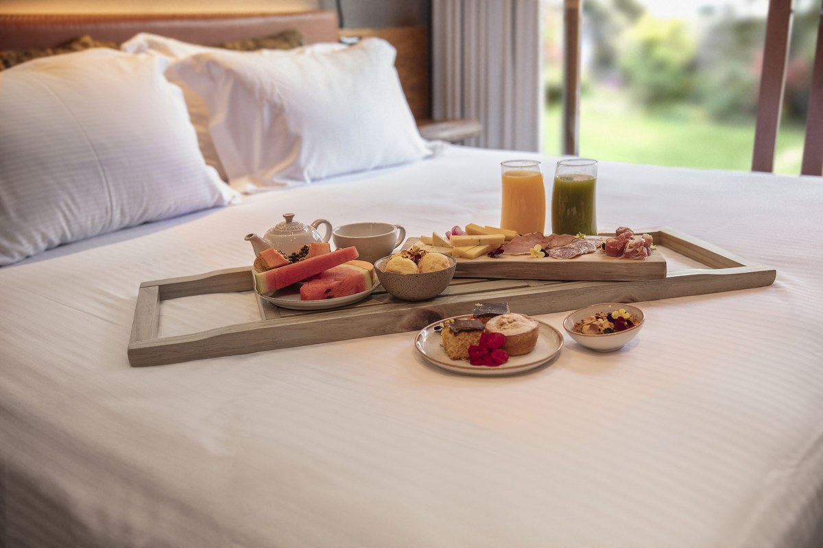 Bandeja de café da manhã luxuoso na cama com frutas, sucos e charcuteria