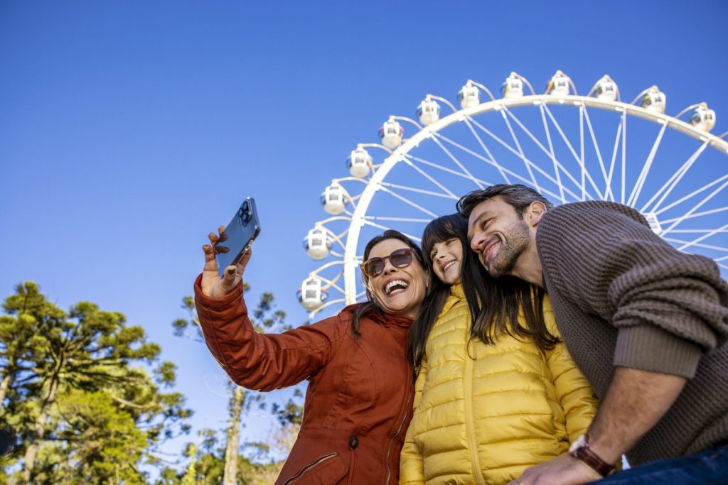 Família tirando selfie na frente da roda-gigante de Gramado em dia de céu azul