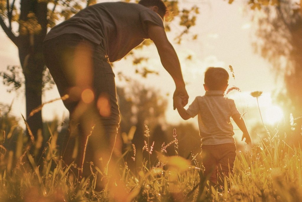 Pai e filho de mãos dadas em campo dourado ao pôr do sol